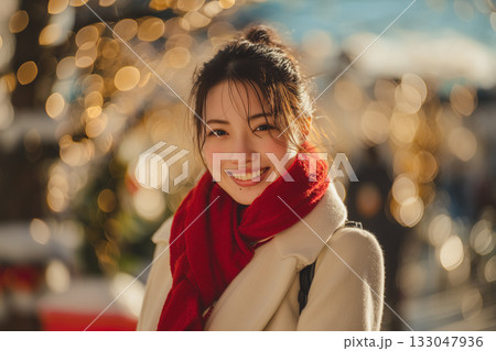 夕暮れの街で微笑む女性｜冬のイルミネーションと赤いマフラーが彩るあたたかなひととき 133047936
