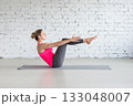 Pilates, boat pose with bent knees. Fit Caucasian woman practice yoga indoor in loft studio. 133048007