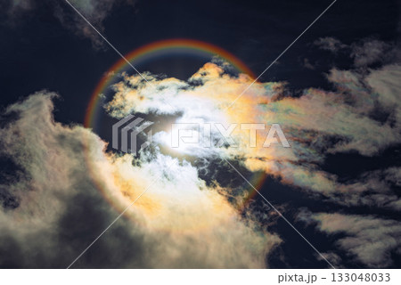 A captivating rainbow solar halo phenomenon with the sun centered in a circular rainbow against a cloudy sky A captivating rainbow solar halo phenomenon with the sun centered in a circular rainbow against a cloudy sky 133048033