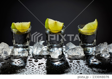 Tequila shots with lime slices on a wet black table. 133048076