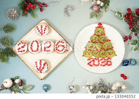 Christmas and New Year dishes. Curd muffins with pomegranates in glaze with numbers 2026 and a kiwi tree for a festive table, an idea for decorating food and decorating New Year dishes for children 133048352