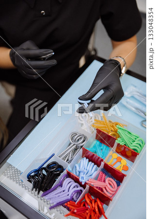 Orthodontic elastics and power chains selected with pliers in dental clinic, closeup Orthodontic elastics and power chains selected with pliers in dental clinic, closeup 133048354