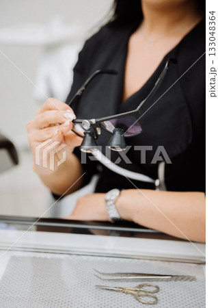 Clinician holding dental loupes for precision work, with tools on table, clinic closeup 133048364