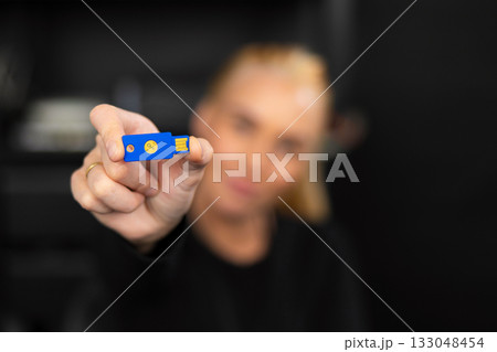 Caucasian woman IT security technician in a tech office holding a blue USB flash drive for data security 133048454