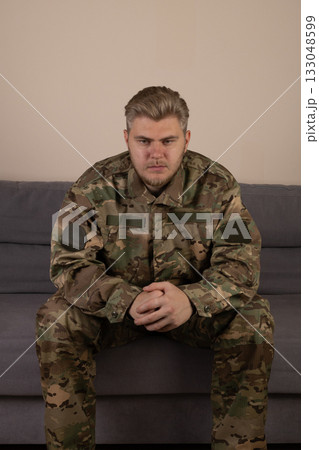 a man in a military uniform sitting on a sofa, looking down 133048599