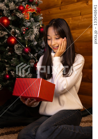 The woman is opening a Christmas present near the Christmas tree The woman is opening a Christmas present near the Christmas tree 133048641
