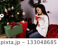 woman is enjoying a hot drink from a red mug next to a decorated Christmas tree 133048685