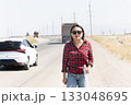 A woman walks along a road next to a white car 133048695