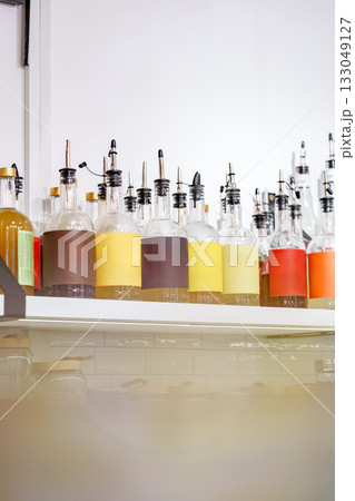 Colorful bottles with various liquids displayed on a shelf in a bright cafe setting 133049127