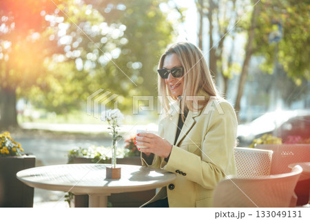Woman enjoying coffee outdoors on a sunny day in a lively urban setting 133049131