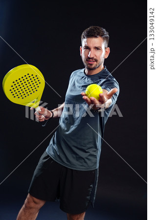Player prepares to serve a bright yellow ball with a paddle in a dark setting 133049142