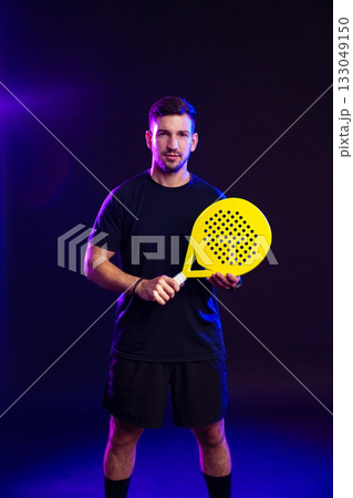 Man holding a yellow paddle racket in a dimly lit setting with colorful lights 133049150