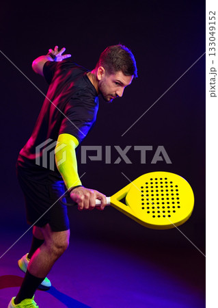 Player practicing with a yellow paddle in a colorful sports studio at night 133049152