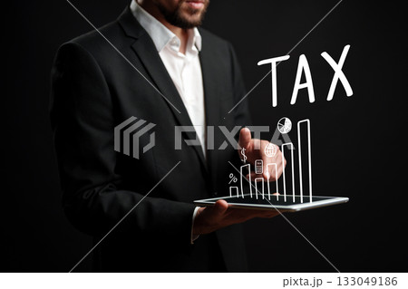 Businessman presenting tax data on tablet with graphs and symbols during a dark background 133049186