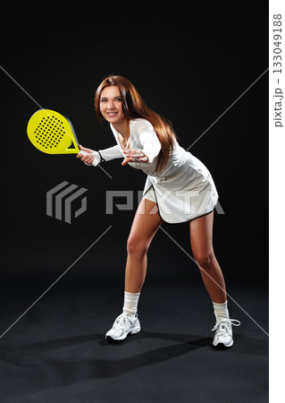 Woman playing paddle tennis indoors wearing white sports attire with a yellow paddle Woman playing paddle tennis indoors wearing white sports attire with a yellow paddle 133049188