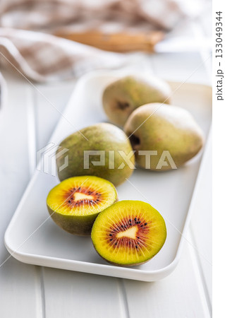 Red kiwi fruit on plate on white table. Red kiwi fruit on plate on white table. 133049344