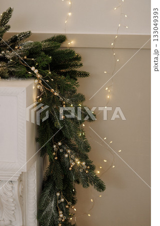 Christmas garland with lights and pearls on white fireplace and beige wall Christmas garland with lights and pearls on white fireplace and beige wall 133049393