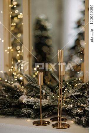 Golden candle holders on festive mantel with fir branches and lights in cozy room 133049394