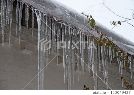 Cold winter, ice formation. Big icicles hang from roof of house 133049427