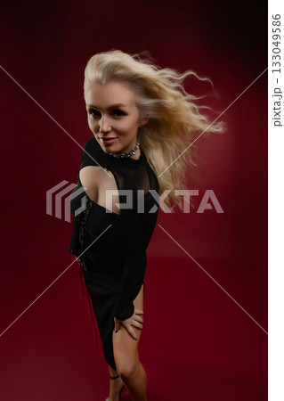 Young woman posing confidently in a stylish black dress against a vibrant red background 133049586