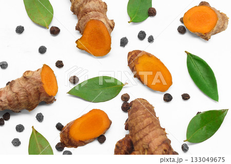 Herbal Ingredients. Sliced turmeric roots with green leaves and black peppercorns on a white background. Herbal Ingredients. Sliced turmeric roots with green leaves and black peppercorns on a white background. 133049675