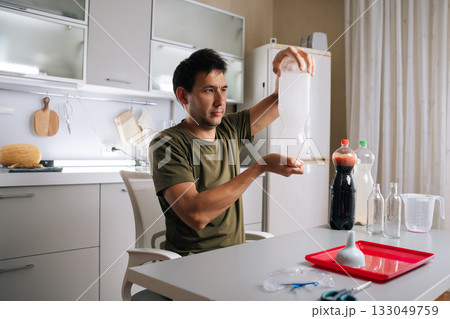 Home gardening enthusiast male mixing homemade liquid fertilizer in kitchen, using bottles, water and other ingredients, demonstrating sustainable approach to plant care. Concept of indoor farming 133049759