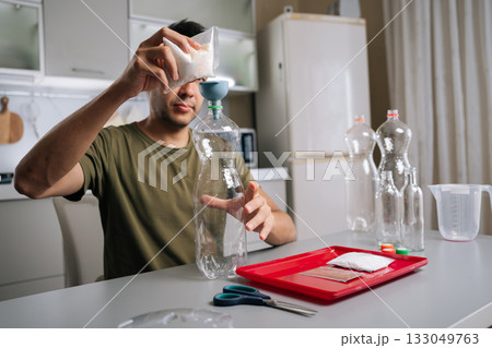 Portrait of gardener pouring fertilizer from bag into plastic bottle using funnel, preparing nutrients for plants, demonstrating sustainable approach to gardening and plant care. Portrait of gardener pouring fertilizer from bag into plastic bottle using funnel, preparing nutrients for plants, demonstrating sustainable approach to gardening and plant care. 133049763