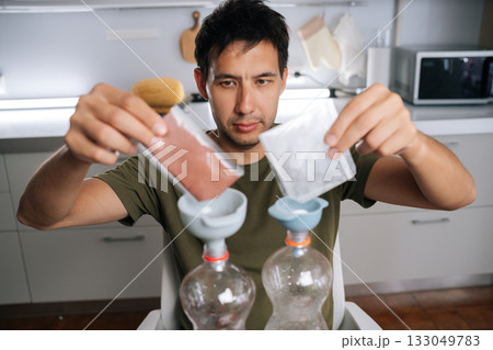 Urban farmer male pouring two different types of fertilizer from small bags into measuring cups, preparing plant nutrients in modern home kitchen. Concept of healthy sustainable cultivation Urban farmer male pouring two different types of fertilizer from small bags into measuring cups, preparing plant nutrients in modern home kitchen. Concept of healthy sustainable cultivation 133049783