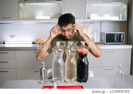 Chemist wearing safety glasses carefully preparing fertilizer for plants in kitchen, using various liquids and bottles, ensuring mixture safe and effective for promoting plant growth. Chemist wearing safety glasses carefully preparing fertilizer for plants in kitchen, using various liquids and bottles, ensuring mixture safe and effective for promoting plant growth. 133049785