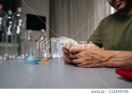 Close-up hands of gardening enthusiast wearing protective eyewear measuring nutrient solution for vertical hydroponic setup, maximizing plant health and productivity in compact indoor growing space 133049786