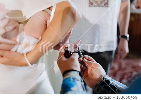 Priest anoints newborns foot during baptism ceremony, close up of sacred christening ritual Priest anoints newborns foot during baptism ceremony, close up of sacred christening ritual 133050459