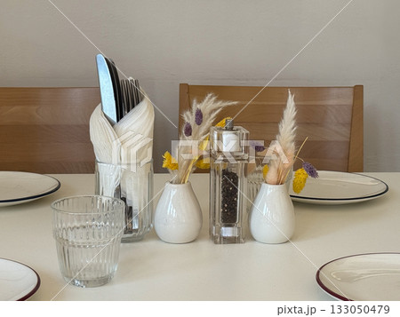 Table arrangement with cutlery, glassware, and dried flowers. Cozy minimalist cafe atmosphere, attention to detail, and warm daylight mood. 133050479