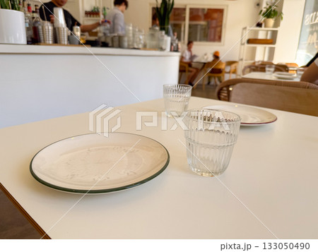 Table view towards cafe counter and guests in soft daylight. Social atmosphere, design harmony, and everyday lifestyle. Table view towards cafe counter and guests in soft daylight. Social atmosphere, design harmony, and everyday lifestyle. 133050490