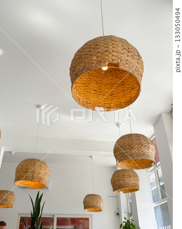 Woven pendant lamps hanging from white ceiling. Natural materials, Scandinavian simplicity, and cozy lighting design. 133050494