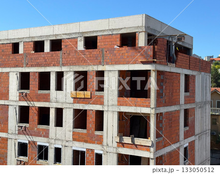 Unfinished brick apartment building under clear blue sky. Urban development, construction progress, and architectural growth. 133050512
