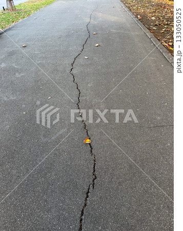 Cracked asphalt surface with visible damage lines. Urban decay, infrastructure wear, and passage of time. 133050525