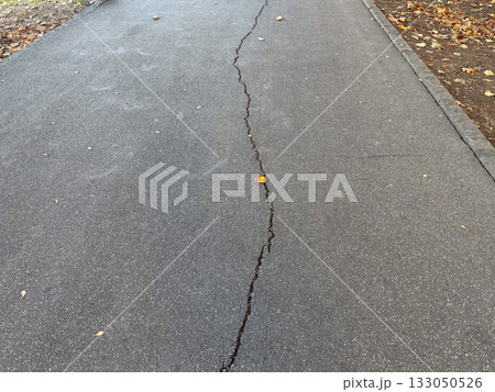 Cracked asphalt surface with visible damage lines. Urban decay, infrastructure wear, and passage of time. Cracked asphalt surface with visible damage lines. Urban decay, infrastructure wear, and passage of time. 133050526