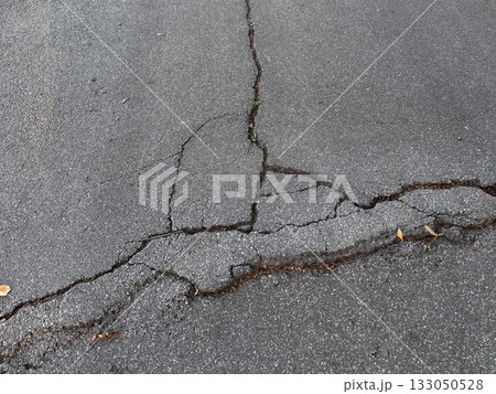 Cracked asphalt surface with visible damage lines. Urban decay, infrastructure wear, and passage of time. 133050528