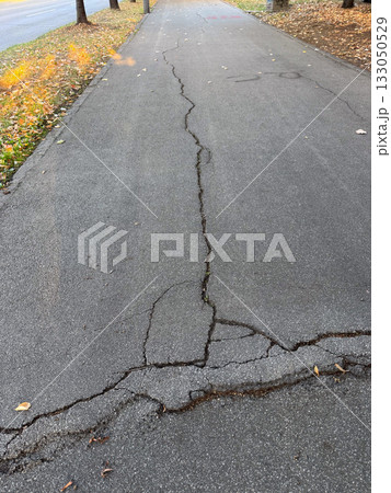 Cracked asphalt surface with visible damage lines. Urban decay, infrastructure wear, and passage of time. 133050529