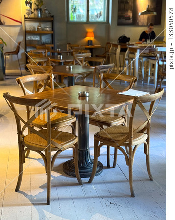 Empty cafe interior with wooden tables and chairs in soft daylight. Calm atmosphere, hospitality, and anticipation of social interaction. Empty cafe interior with wooden tables and chairs in soft daylight. Calm atmosphere, hospitality, and anticipation of social interaction. 133050578