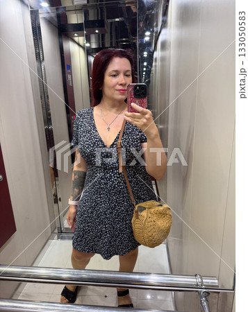 Woman taking mirror selfie inside elevator with casual summer outfit. Modern lifestyle, confidence, and expression of individuality in everyday routine. 133050583