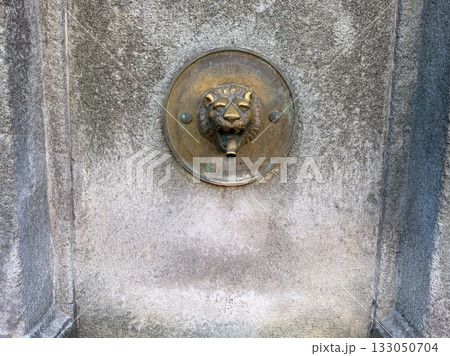 Decorative lion head fountain spout on stone wall. Historic architecture, craftsmanship, and symbolic expression of power and culture. 133050704