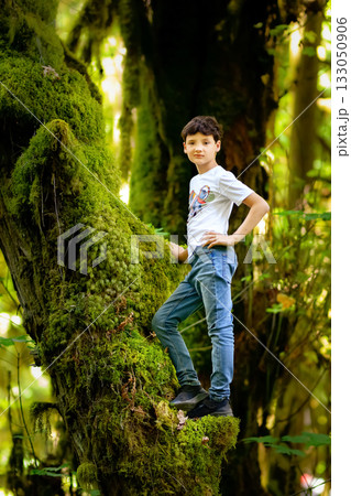 Teen boy is standing on the mossy tree trunk in the rainforest. 133050906