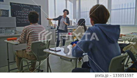 Female Teacher Stands Near Blackboard Explaining Coding Assignment to Group of Students in Bright Classroom 133051597