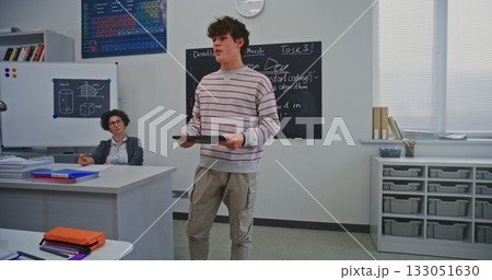 Young Male Student Stands at Front Classroom, Holding Digital Tablet While Delivering Report 133051630