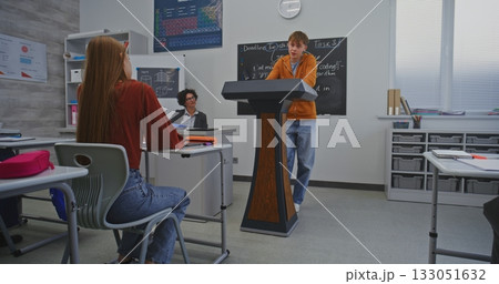 Student in Orange Hoodie Stands Behind Podium in Front of Classmates and Speaks Confidently 133051632