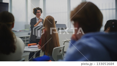 Confident Female Instructor Teaches Coding to Attentive Students, Pointing Lines Code on Display 133051684