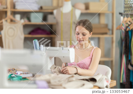 Young seamstress sews a dress on a machine Young seamstress sews a dress on a machine 133053467