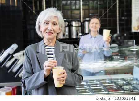Smiling senior lady drinking refreshing bubble tea in disposable cup 133053541
