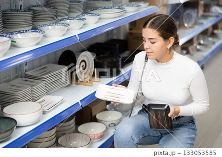 Young girl choosing square ceramic plates on shelves at Asian store Young girl choosing square ceramic plates on shelves at Asian store 133053585
